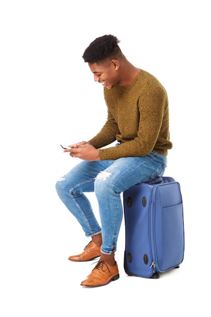 jeune homme de voyage afro-américain assis sur une valise avec un téléphone portable