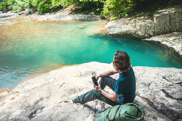 Jeune homme voyageur avec sac à dos relaxant sur les rochers du lac de montagne Paysage d'été