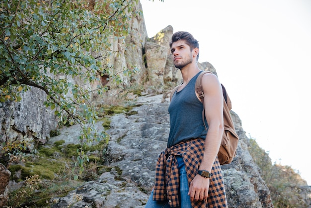 Jeune homme voyageur avec sac à dos sur rocher. de l'image ci-dessous