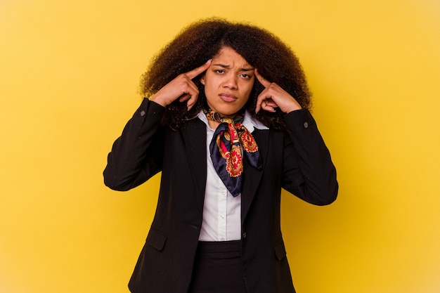 Jeune hôtesse de l'air afro-américaine isolée sur jaune concentrée sur une tâche, gardant les index pointés vers la tête.