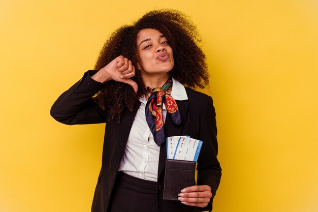 Jeune hôtesse de l'air afro-américaine tenant un billet d'avion isolé sur un mur jaune se sent fier et confiant, exemple à suivre.