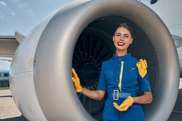 jeune hôtesse de l'air caucasienne s'appuyant d'une main sur le turboréacteur