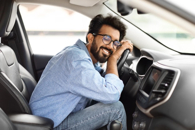 Un jeune Indien enthousiaste étreint le volant d'une nouvelle voiture.