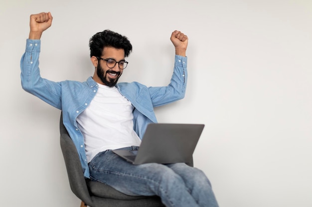 Un jeune Indien heureux utilisant un ordinateur portable et célébrant son succès