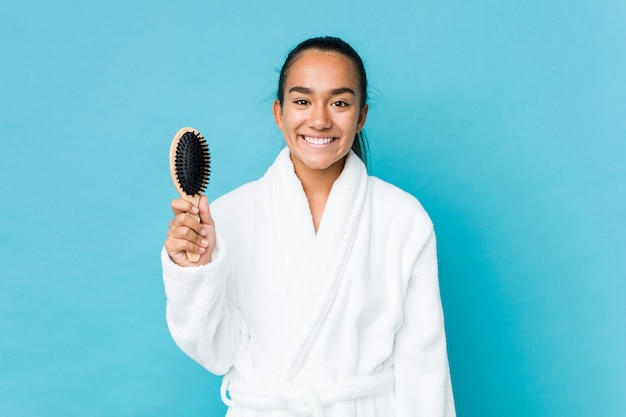 Jeune Indien de race mixte tenant une brosse à cheveux heureux, souriant et gai.