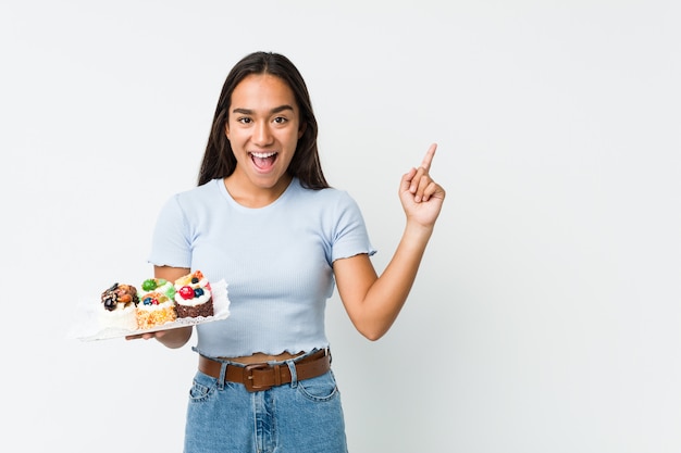 Jeune Indien de race mixte tenant un gâteaux sucrés souriant joyeusement pointant avec l'index loin.