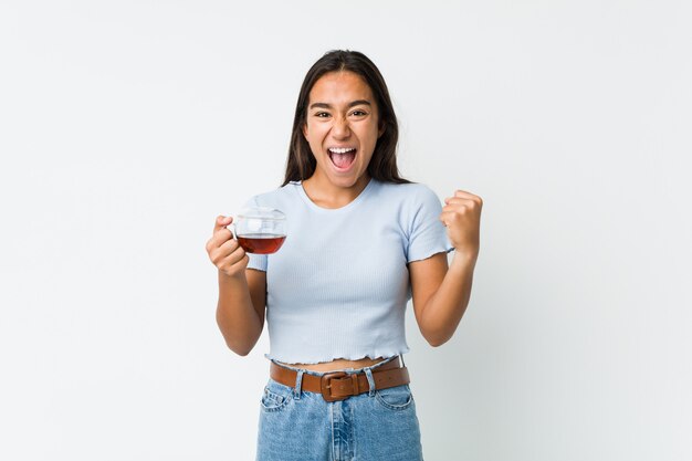 Jeune Indien de race mixte tenant une tasse de thé acclamant sans soucis et excité