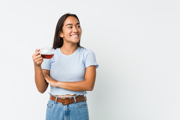 Jeune Indien de race mixte tenant une tasse de thé souriant confiant avec les bras croisés.