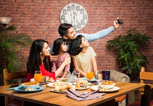 Jeune indienne Famille de quatre personnes mangeant de la nourriture à table à la maison ou au restaurant. Mère, père et deux filles sud-asiatiques prenant un repas ensemble