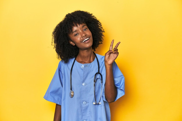 Jeune infirmière afro-américaine en studio avec fond jaune joyeuse et insouciante