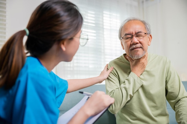 Une jeune infirmière asiatique vérifie la douleur au cou d'un homme âgé dans une clinique d'une maison de retraite. Une femme médecin examine les ganglions lymphatiques du cou pour déterminer si le mal de gorge est gonflé.