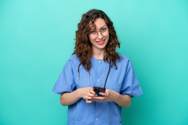Jeune infirmière caucasienne femme isolée sur fond bleu envoyant un message avec le mobile