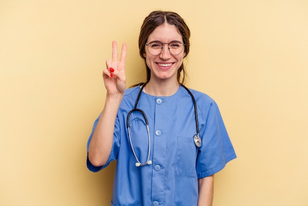 Jeune infirmière caucasienne femme isolée sur fond jaune montrant le numéro deux avec les doigts.