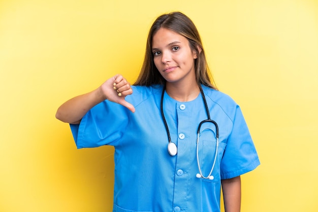 Jeune infirmière caucasienne femme isolée sur fond jaune montrant le pouce vers le bas avec une expression négative