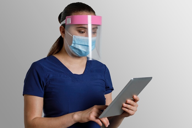 Jeune infirmière latine avec masque et écran facial à l'aide d'une tablette numérique