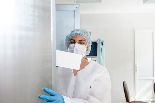 Une jeune infirmière portant un masque de protection et des gants prend des documents dans un casier du centre médical ...