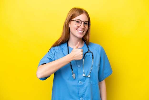 Jeune infirmière rousse femme isolée sur fond jaune donnant un geste du pouce levé