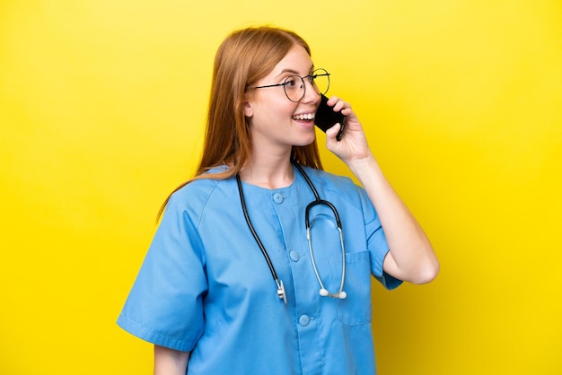 Jeune infirmière rousse femme isolée sur fond jaune en gardant une conversation avec le téléphone mobile