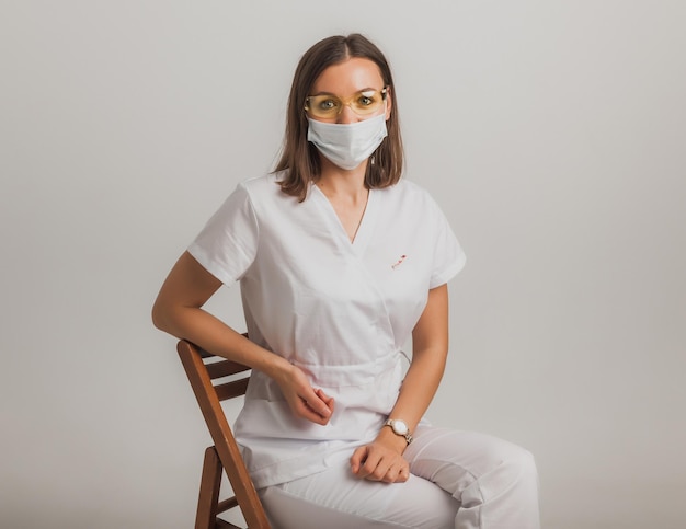 Jeune infirmière en uniforme médical blanc et en masque médical et lunettes portrait en studio isolé.