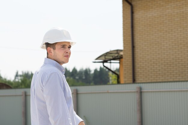 Un jeune ingénieur civil masculin portant un casque blanc visite le site pour voir les progrès de la construction