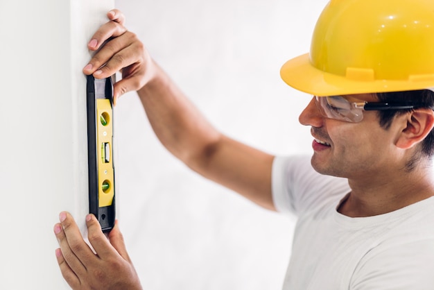 Jeune ingénieur en construction dans un casque jaune travaillant et prenant des mesures sur le mur au chantier de construction