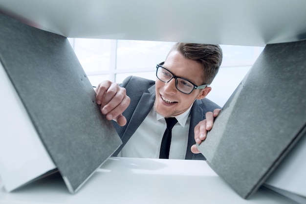 Un jeune ingénieur souriant sélectionne des documents sur une étagère dans un placard