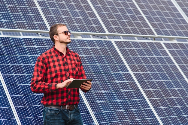 Jeune ingénieur avec tablette tactile debout près de panneaux solaires à l'extérieur