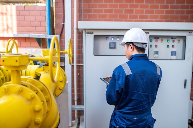 Jeune ingénieur travaillant dans une grande usine Technicien en uniforme de protection et avec casque vérifiant la température dans les tuyaux Lire la pression sur le distributeur de pression