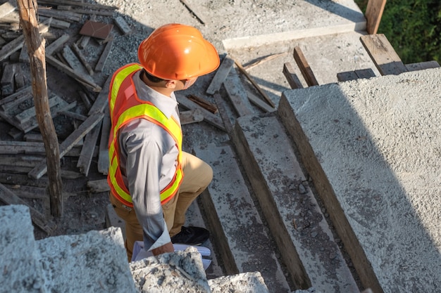 Photo jeune ingénieur travailleur en casque de protection et papier de plans inspecter l'intérieur du bâtiment au chantier de construction