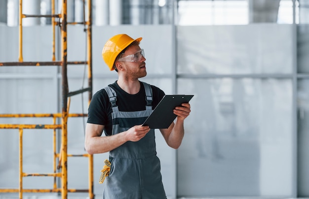 Jeune Ingénieur En Uniforme Gris Avec Bloc-notes Travaille à L'intérieur Dans Un Grand Bureau Moderne Pendant La Journée