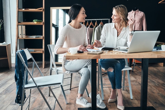 Jeune et intelligent. Belles jeunes femmes travaillant ensemble et souriantes assises dans l'atelier