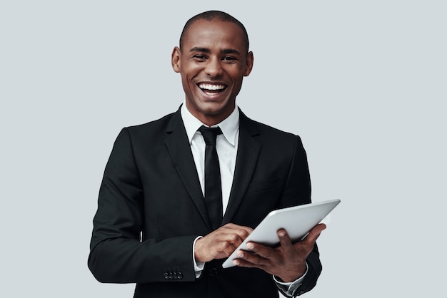 Jeune et intelligent. Jeune homme africain en tenue de soirée regardant la caméra et souriant en se tenant debout sur fond gris