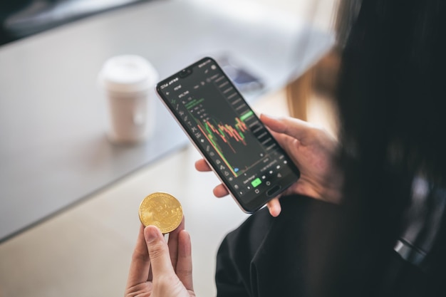 Une jeune investisseur commerçante asiatique détient un bitcoin d'or à l'aide d'un téléphone portable pour échanger du bitcoin