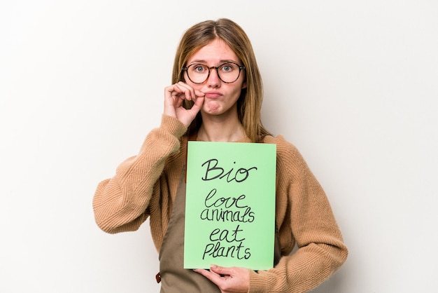 Jeune jardinier femme tenant une pancarte bio isolée sur fond blanc avec les doigts sur les lèvres en gardant un secret