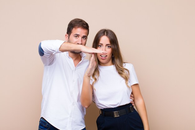 Jeune joli couple contre un mur plat beige