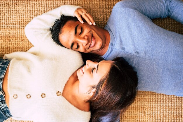 Jeune joli couple interracial s'allonger sur le tapis et sourire en prenant soin et l'amour de chacun