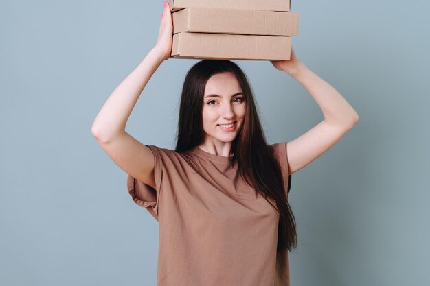 Jeune jolie belle femme joyeuse tenant au-dessus de sa tête une pile de boîtes les portant