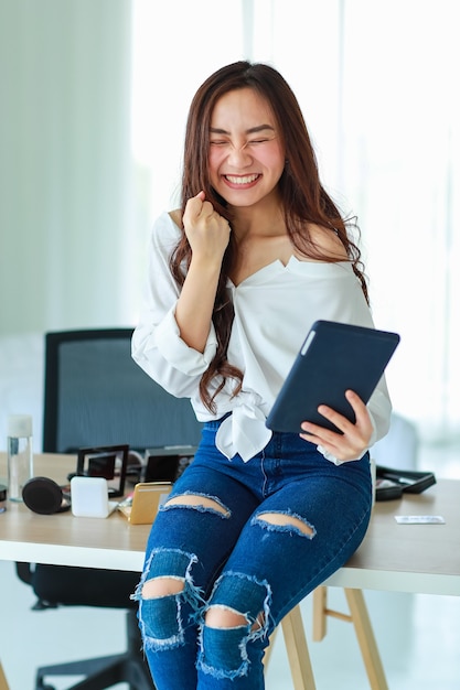 Jeune, jolie et belle vendeuse asiatique tenant une tablette et les yeux fermés avec ravissante et excitée après avoir vu la commande du client. Vente sur Internet et concept de marketing en ligne