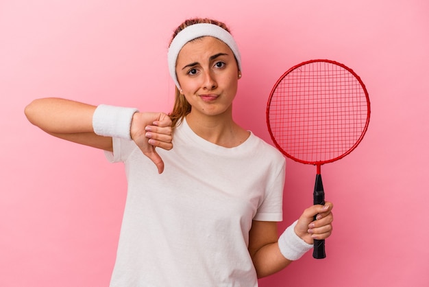 Jeune jolie blonde caucasienne femme tenant une raquette de badminton isolée sur un mur rose montrant un geste d'aversion, les pouces vers le bas