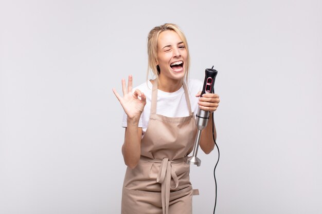 Jeune jolie blonde femme boulanger avec un mixeur