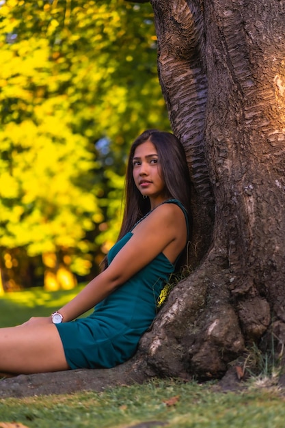 Une jeune jolie brune latina aux longs cheveux raides appuyée contre un arbre