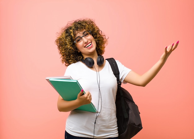 Jeune jolie étudiante à l'air heureuse, arrogante, fière et satisfaite, se sentant comme un numéro un contre le mur rose