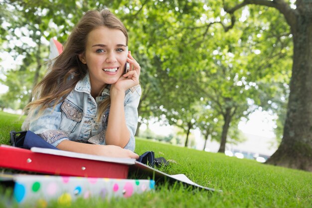 Jeune jolie étudiante allongée sur l&#39;herbe au téléphone