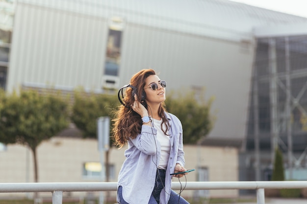 Jeune jolie étudiante en attente d'une voiture de taxi et écouter de la musique