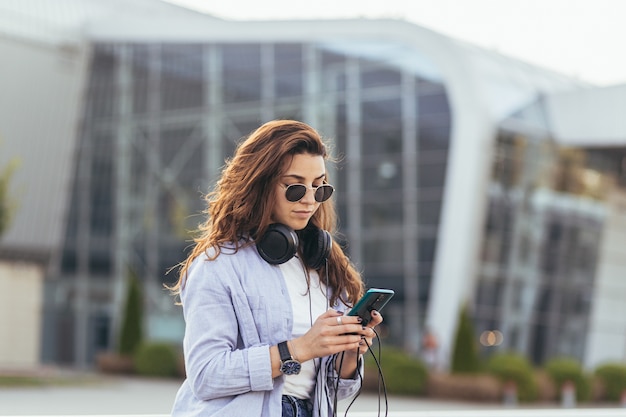 Jeune jolie étudiante en attente d'une voiture de taxi et écouter de la musique