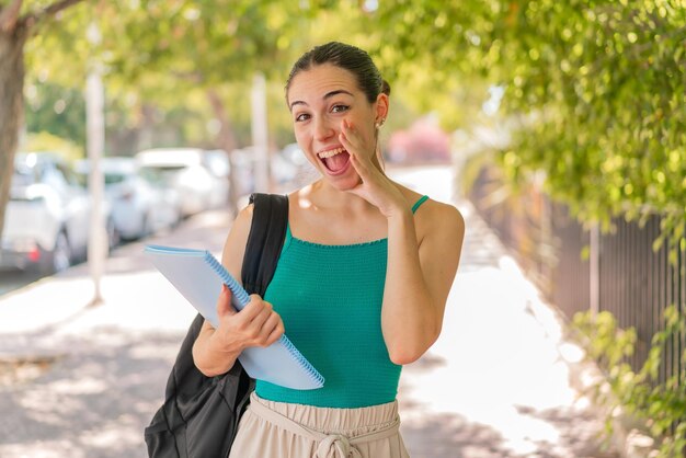 Jeune jolie étudiante à l'extérieur criant avec la bouche grande ouverte