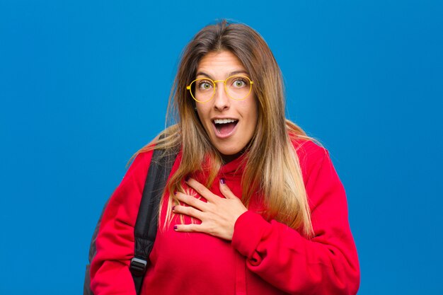 Jeune jolie étudiante se sentant choquée et surprise, souriante, prenant la main à cœur, heureuse d’être la seule ou montrant de la gratitude