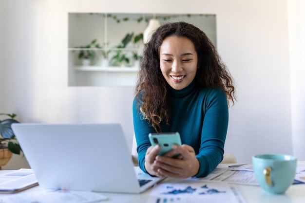 Jeune jolie femme d'affaires asiatique au bureau assise sur une chaise de bureau à l'aide de son smartphone