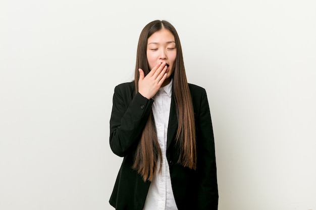 Jeune jolie femme d'affaires chinoise bâillant montrant un geste fatigué qui couvre la bouche avec la main.