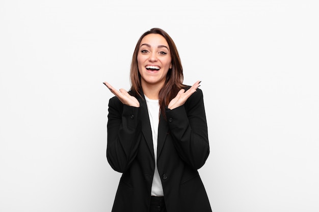 Jeune jolie femme d'affaires heureux et excité, choqué par une surprise inattendue avec les deux mains ouvertes à côté de face contre le mur blanc